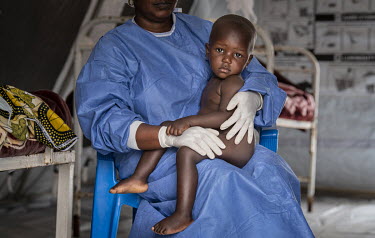 Nurse Eugenie Kabuya with Sandrine (22 months) sits on the lap of a woman in the UNICEF creche at the Ebola Treatment Centre in Butembo. Sandrine's mother is seriously unwell with Ebola although Sandr...