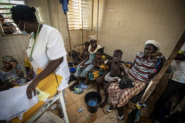 A member of the medical staff at the Kaya Regional Hospital reads the case notes for some children sitting with their guardians on a bed behind her. The hospital is operating at over 100% capacity, in...