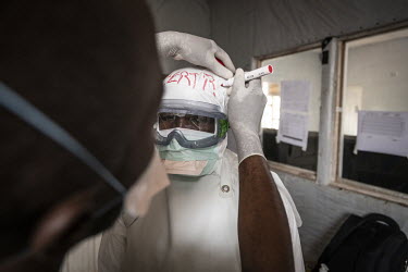 A colleague writes hygienist Bertrand Karumba's (33) name on his personal protective equipment as he prepares to enter the Ebola treatment centre's treatment area.  An Ebola outbreak was declared on 7...