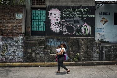A woman carries her child past an anti-abortion mural, one of multiple visual signs of the religious and anti-abortion tendency in the country. The mural is painted on a private house close to a prima...