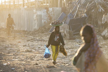 A Fulani woman walks through an IDP camp carrying a tray of avocados on her head.  Thousands of Fulani (semi-nomadic herders of the Sahel) have been displaced by fighting with the Dogon people and hav...