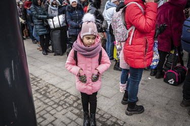 A child wearing a pink coat waiting among a crowd of refugees at Lviv Central railway station.