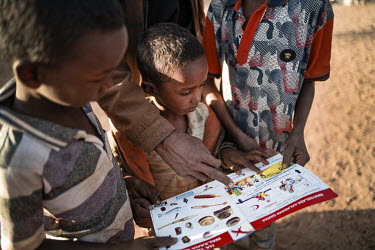 Children look at an explosive ordnance risk education flyer. Their father Abdi, said: ''This was a fighting area before and we knew there were dangers. I told the children all the time to be careful a...