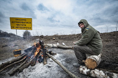A man warms himself by a fire near to where members of the Territorial Defence Forces are building defensive fortifications east of Ternopil.