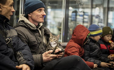 A man holding a pet cat sits with refugees from Mauriupol at a makeshift reception centre in a Zaporizhzhia supermarket.