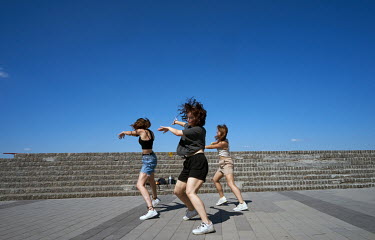 Young women practice dancing during sunny weather on Naberezhnaya Street.