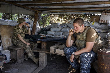 Ukrainian soldiers smok under a camouflaged shelter at a frontline position near Donetsk city.