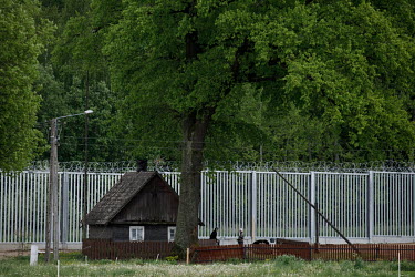 An old wooden house stands beside the new border fence built between Poland and Belarus.  In the autumn of 2021 there were clashes between Polish police and migrants trying to cross the Polish border...