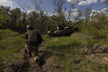A Ukrainian soldier crouches near an abandoned Russian tank on the banks of the Seversky Donets river. Earlier in May 2022, Ukrainian forces had inflicted heavy losses on a Russian battalion at this l...