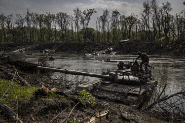 A Ukrainian soldier examines an abandoned Russian tank part submerged in the Seversky Donets river. Earlier in May 2022, Ukrainian forces had inflicted heavy losses on a Russian battalion at this loca...