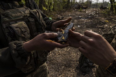 Ukrainian soldiers examine a handgun, salvaged from the Russian soldier's backpack found in an tank abandoned in the Seversky Donets river at the scene of a failed pontoon crossing. Earlier in May 202...