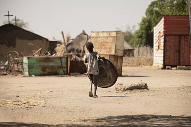 A child carries a large metal basin through the village of Mulbok.