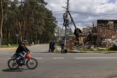 A man rides a bicycle past workers repairing internet cables in the heavily destroyed town of Irpin.