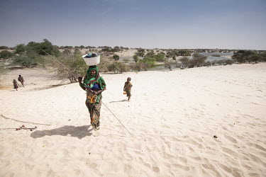 A woman and her child walk on the sand shores that surround Lake Chad.  Lake Chad, which spanned 9,652sqm in 1963, has shrunk by 90 per cent in recent decades. Climate change is to blame, with populat...