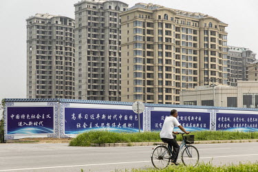 A man rides a bike past residential buildings in Xiongan. Over a year ago, President Xi Jinping designated Xiongan a new high-tech city. Things are off to a slow start, and locals tell of shut down fa...