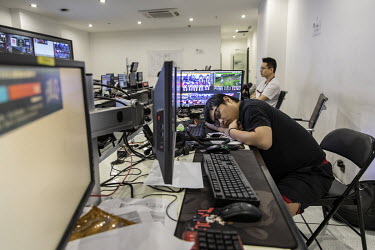 A broadcast worker takes a nap in front of screens before the start of a professional match at an E-game arena.