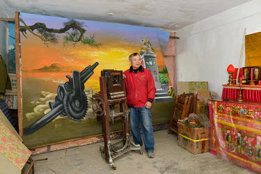Retired photographer Mr. Chen Yi-pan stands beside his studio camera with his favourite hand-painted backdrop, in Tien Ao village. Chen used to make a good living taking portraits of the many ROC troo...