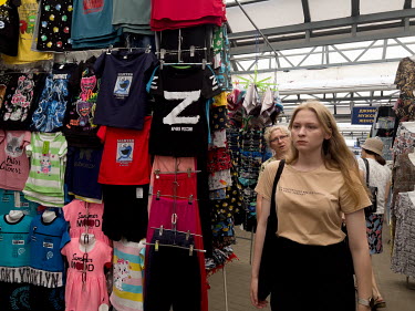 A woman walks past a stall in the central market selling t-shirts including one with the letter 'Z' and 'ARMY OF RUSSIA' written beneath it.