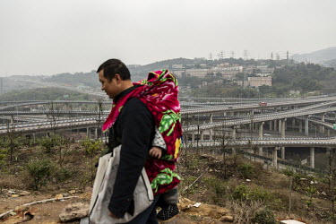 A man carrying a child on his back walks on a hill overlooking an jumble of elevated highways on the outskirts of Chongqing. China's largest municipality by population and land area, Chongqing is cent...