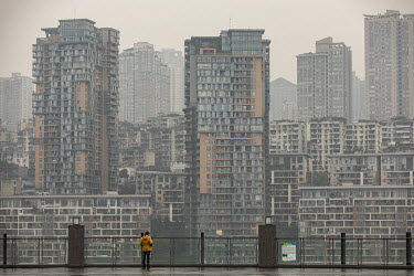 A woman stands on a balcony looking across the Yangtze to highrise apartments on a hill in Chongqing. China's largest municipality by population and land area, Chongqing is central to China's strategy...