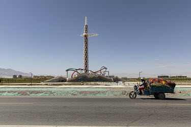 A man drives his rickshaw past a monument in Golmud.