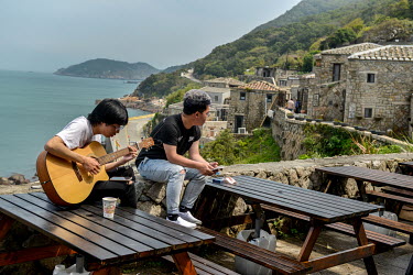 Young Matsu residents playing a guitar while whiling away the time in the ancient and well-preserved traditional Fujianese-style village of Qinbi, a magnet for domestic Taiwanese tourists. March 2022....