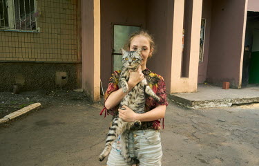 Katya (11) with her cat in front of her block of flats. Due to extensive shelling, she lives with her family in a cellar which they have used as a bomb shelter for months.