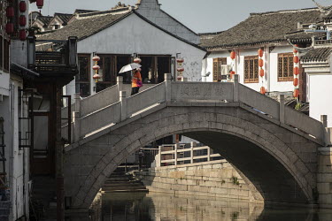 A woman with an umbrella walks over a stone arch bridge in the Zhujiajiao Water Town in Shanghai. Zhujiajiao is one of several canal based towns in the Yangtze Delta region that many tourists visit.