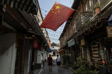 A couple with shopping walk under a Chinese national flag in a narrow alley in the Zhujiajiao Water Town in Shanghai. Zhujiajiao is one of several canal based towns in the Yangtze Delta region that ma...