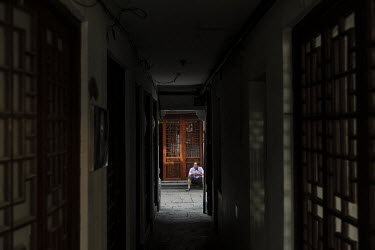 A man sits at the end of a narrow corridor, in front of an traditional wooden door in the Zhujiajiao Water Town in Shanghai. Zhujiajiao is one of several canal based towns in the Yangtze Delta region...