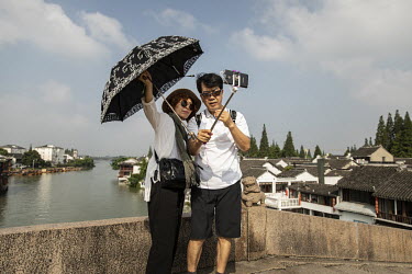 A couple with an umbrella take a selfie while standing on a bridge in the Zhujiajiao Water Town in Shanghai. Zhujiajiao is one of several canal based towns in the Yangtze Delta region that many touris...