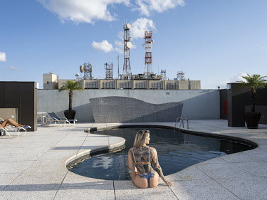 A woman with a tattoo of a skull on her back sits at the edge of the rooftop swimming pool of St Paul Plaza Hotel.