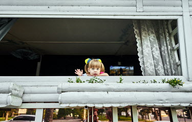A girl with ponytails tied with blue and yellow bows, the colours of Ukrainian flag, waves to passers-by.