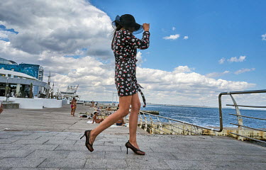 A woman walks on high heels on the Langeron Beach promenade while others sun bathe despite Russia's war.
