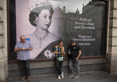 People check their mobile phones while standing in front of a giant image showing the young Queen Elizabeth II displayed in Piccadilly Circus following her death in Scotland on the 8 September 2022 at...