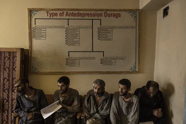 Drug users, who have been caught in the streets by the the Taliban, sit beneath an old sign listing various anti-depression medications as they wait to be seen by staff at the Ibn Sina Drug Addiction...