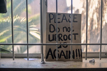 A placard reading 'Please do not uproot us again' stands on a window sill in Cissie Gool House, an abandoned hospital that now houses some 1,000 people. Many of those living there now were initially u...