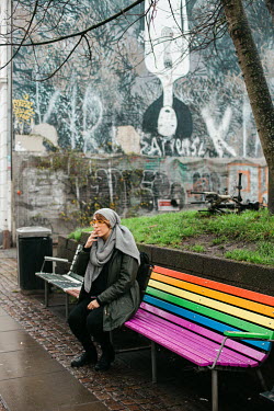Parisa, sits on a bench decorated in the colours of the rainbow flag. She is from the island of Kish, in Iran's Persian Gulf. She now lives in Aarhus. Here she works in her local church, where she is...