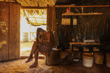 Kamihukalu Kamayura (31) uses her mobile phone while seated sitting next to batteries, powered by solar panels, in her home in Ngosoko village on Wawi Indigenous Land. Thanks to the power provided by...