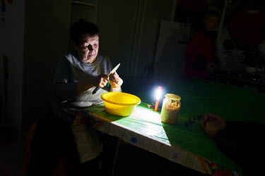 Lyuba peeling potatoes by the light of a torch due to electrical power cuts caused by Russia's targeting of civilian infrastructure.