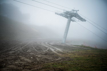 Vehicle tracks scar the land beneath a ski lift pylon on a foggy day during the off season.