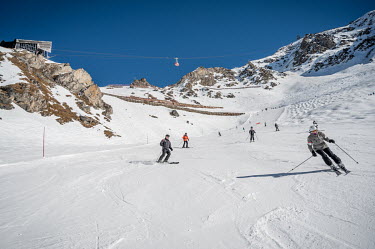 Tourists on a ski slope during winter season. In the background the gondola to the l'Aiguille Rouge carries tourists to an altitude of 3226m.