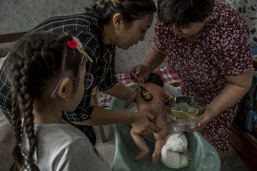 A mother holds her 40-day-old son during the 'Kyrkynan shygaru' ceremony, while a woman, standing in for her deceased mother, purifies the newborn with water in which a silver ring is dipped. 40 days...