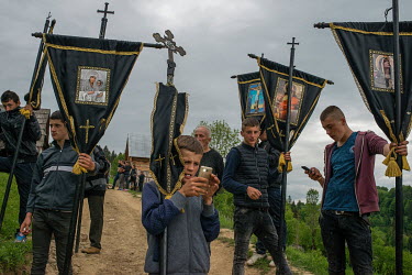 The funeral alley stops for a second and the young boy checks his phone searching for internet coverage. High in the mountains above Poienile de sub Munte, said to be Romania's largest village, is an...