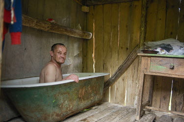 Vasile (56) takes a bath in a bathtub filled with thermal water in a former animal shelter. This natural spring water, rich in minerals, happens to be the only one around and it is inside the property...