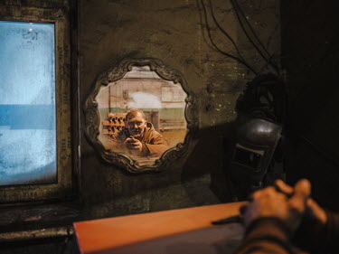 A worker reflected in a mirror at the coal mine's forge, a relic from the past, where equipment from the mining plant is maintained.