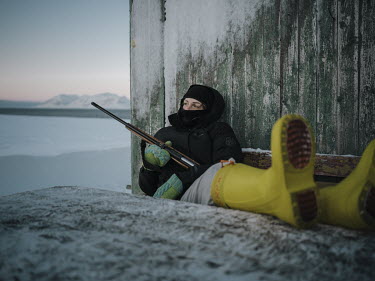 A woman sits outside holding a gun to scare off polar bears.