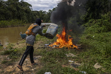 A miner ( garimpeiro ) burns clothes, rubber boots and gallons of fuel abandoned in a clandestine port on the banks of the Uraricoera River during their flight from illegal mining operations in the Ya...