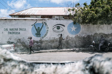 A soldier walks past a wall decorated with a mural with the slogan: 'a nation can be built by its people'.
