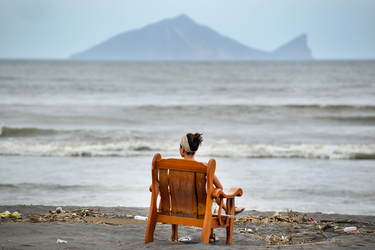 A woman relaxes on a chair on a beach looking towards Turtle Island, on the horizon.
